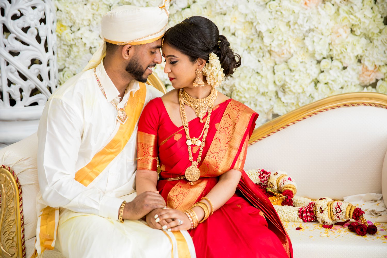 Bride and groom in traditional Hindu wedding garments posing on a love seat.